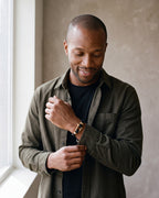 Man in a dark olive overshirt open over a black t-shirt wearing the gold-tone / black Atlas Shackle Bracelet in Braided Leather