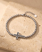 Entire Atlas sideways cross bracelet in silver-tone steel, lying flat on warm stone
