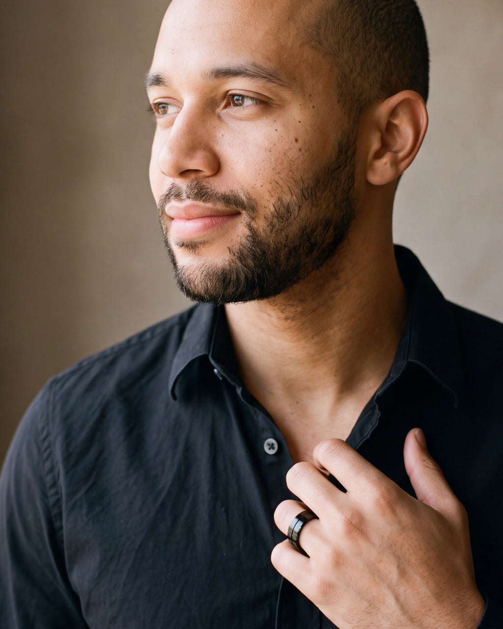 Man in a black shirt looking toward the window, hand on his chest, wearing the black Atlas single groove band ring