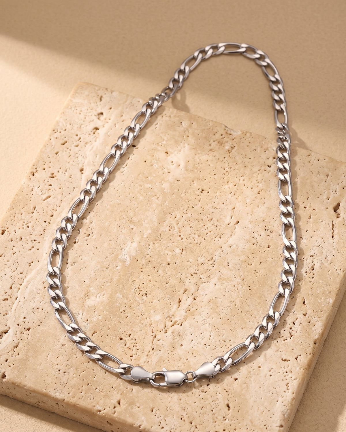 Entire Atlas slim Figaro chain in silver-tone steel, lying flat on warm stone