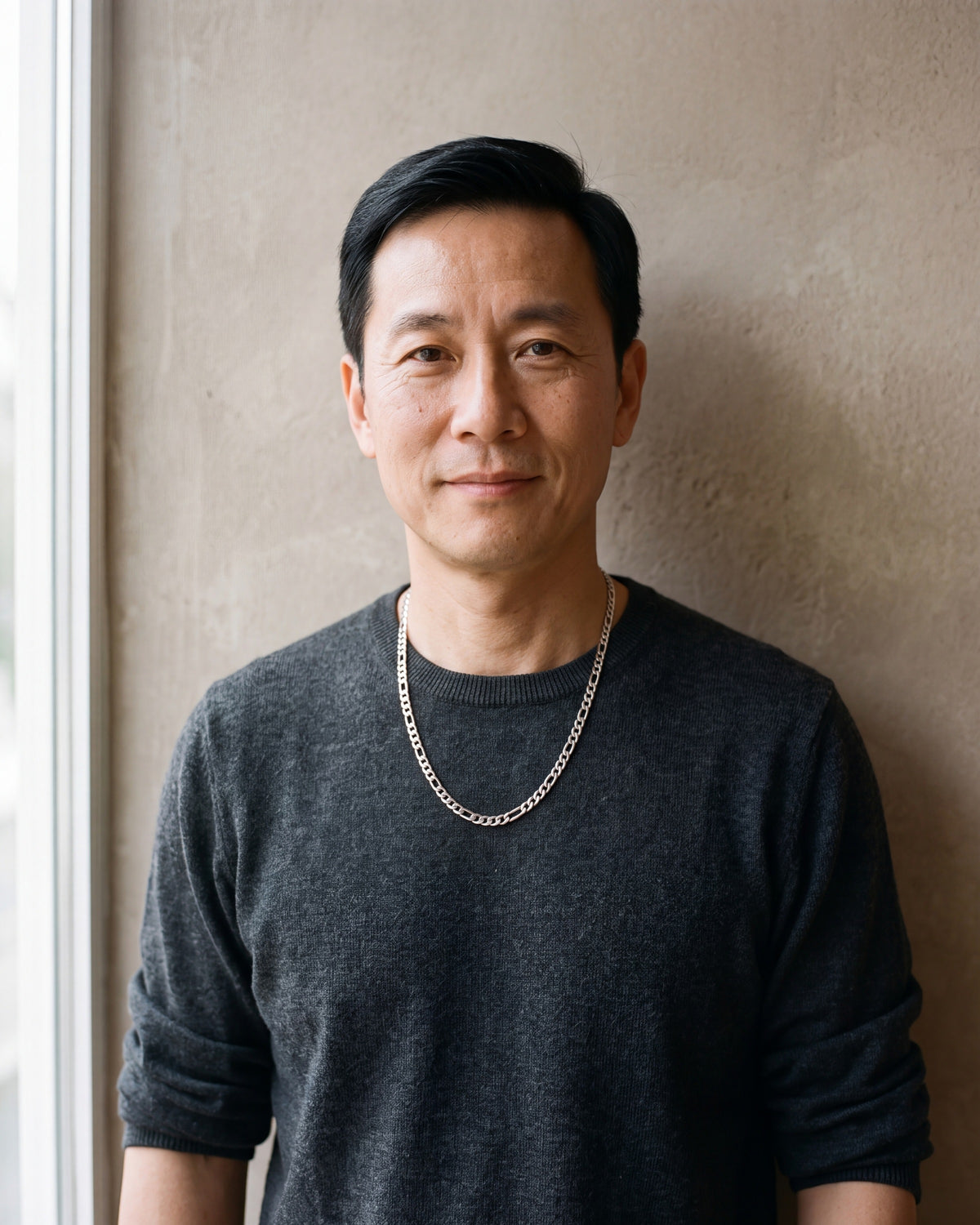 Man in a charcoal knit sweater by a window wearing the Atlas slim Figaro chain in silver-tone steel