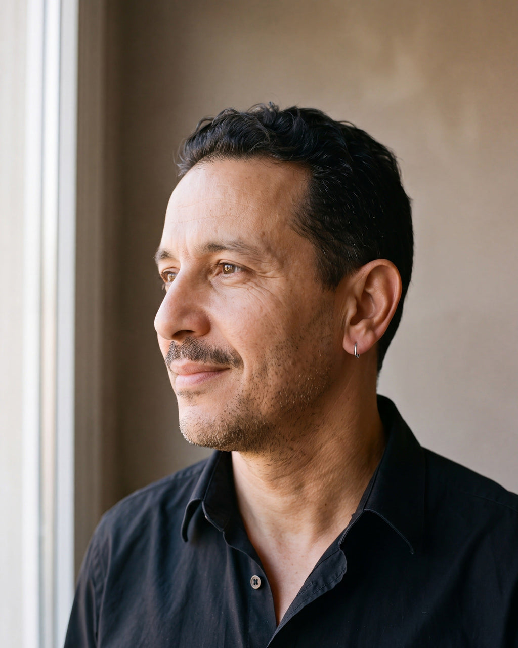 Man in a black shirt by a window wearing a silver-tone Atlas slim hoop earring