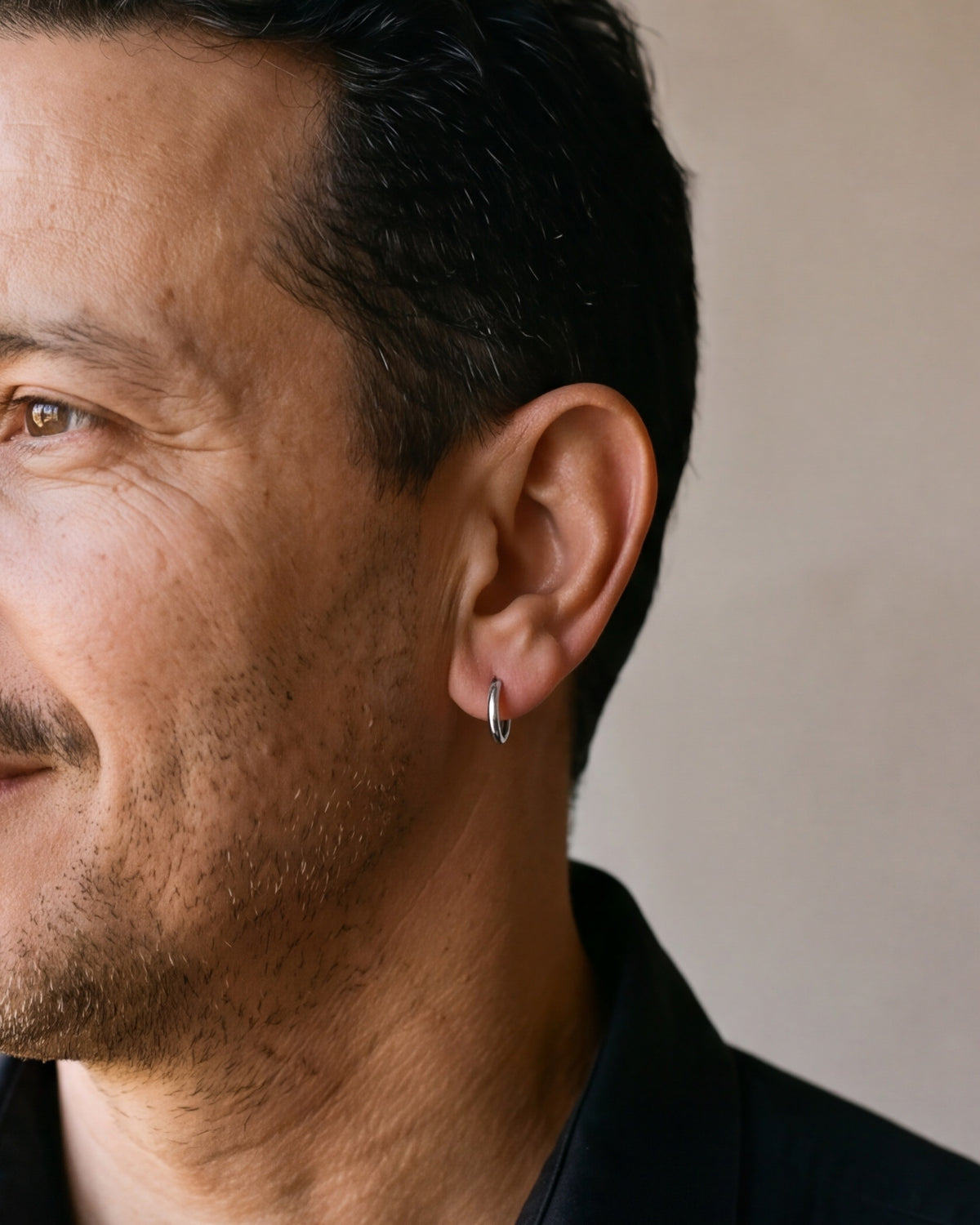 Close-up of the silver-tone Atlas slim hoop earring hugging a man's earlobe