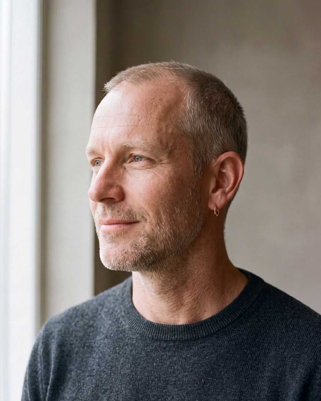 Man in a charcoal sweater by a window wearing a gold-tone Atlas slim hoop earring