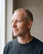 Man in a charcoal sweater by a window wearing a gold-tone Atlas slim hoop earring