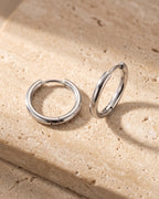 The pair of silver-tone Atlas slim hoop earrings on warm stone