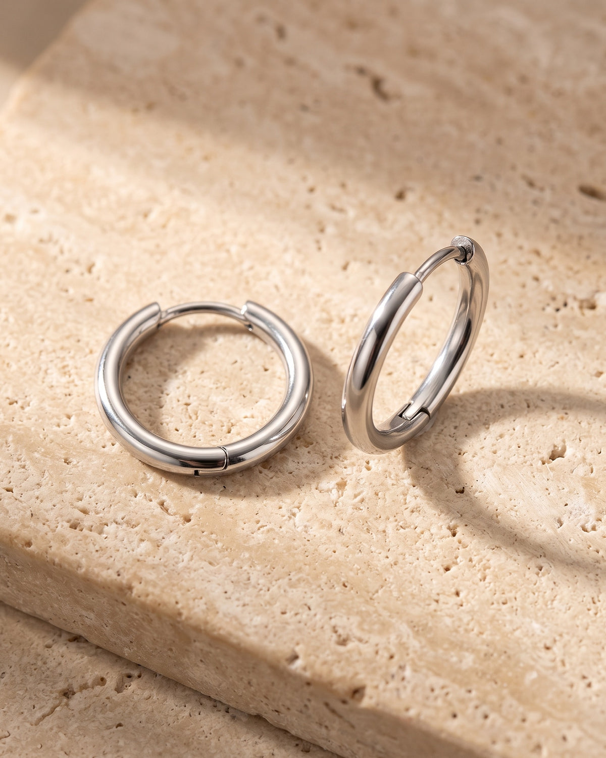 The pair of silver-tone Atlas slim hoop earrings on warm stone