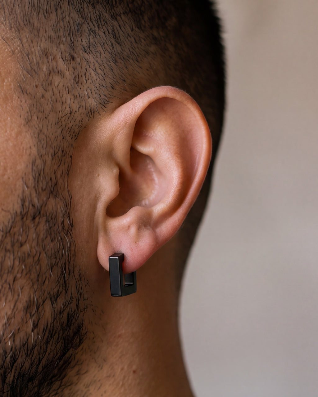 Close-up of the black Atlas square huggie earring hugging a man's earlobe at true size