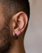 Close-up of the black Atlas square huggie earring hugging a man's earlobe at true size