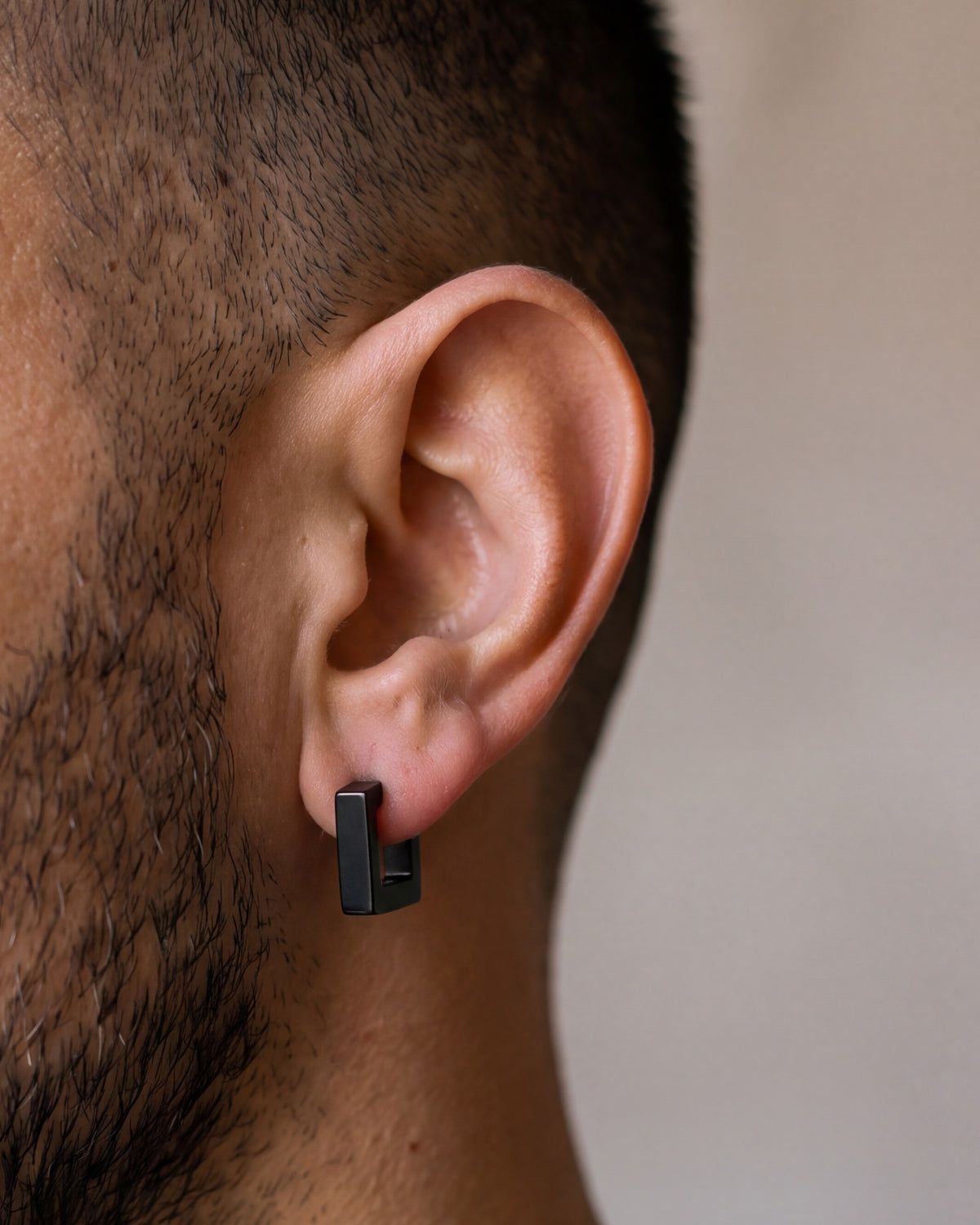 Close-up of the black Atlas square huggie earring hugging a man's earlobe at true size