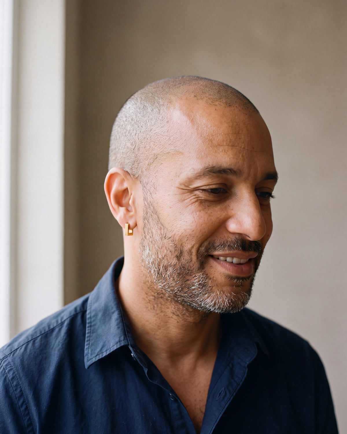 Man in a navy shirt wearing the gold-tone Atlas square huggie earring