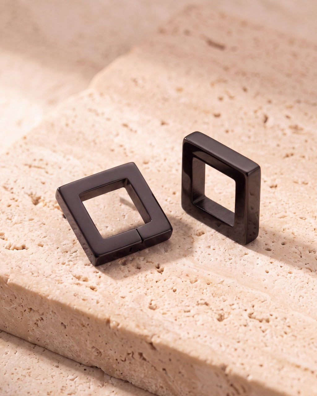 The pair of black Atlas square huggie earrings, both closed, on warm stone