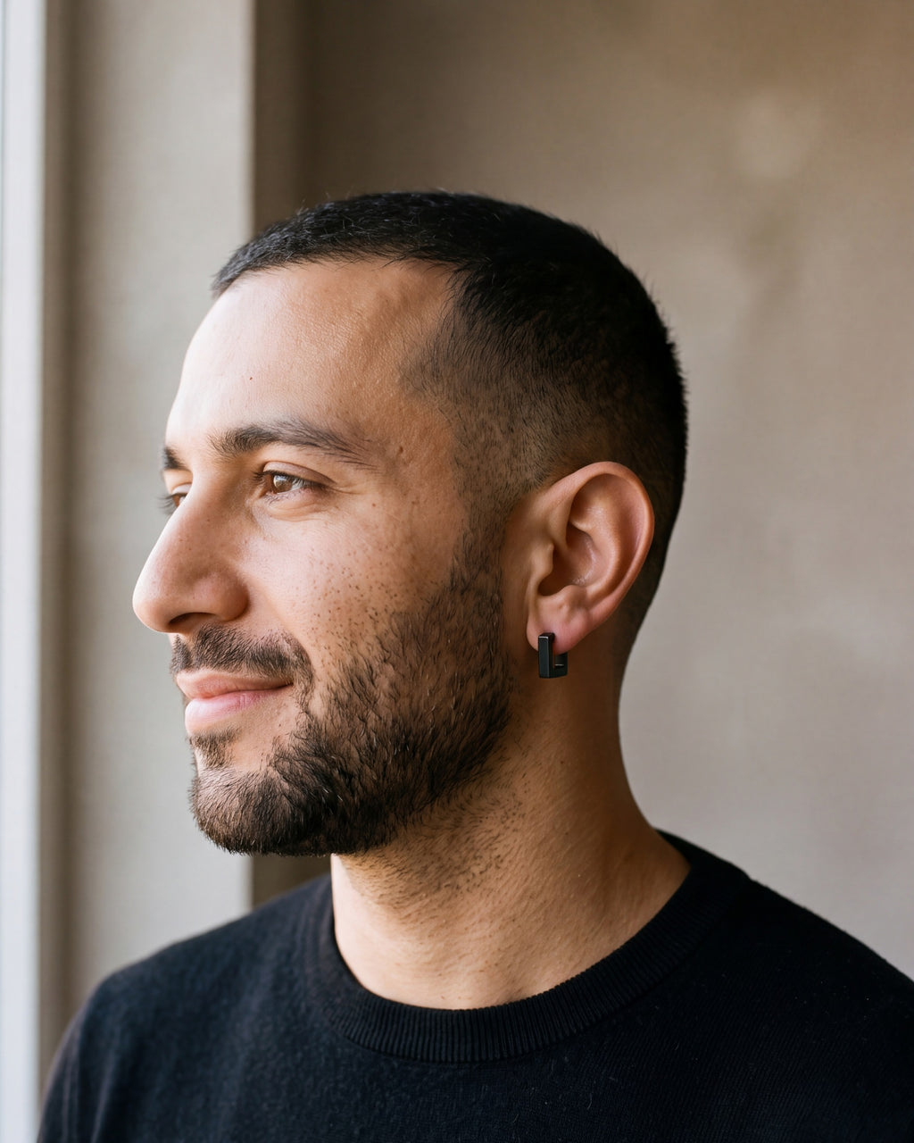 Smiling man in a black knit by a window wearing the black Atlas square huggie earring
