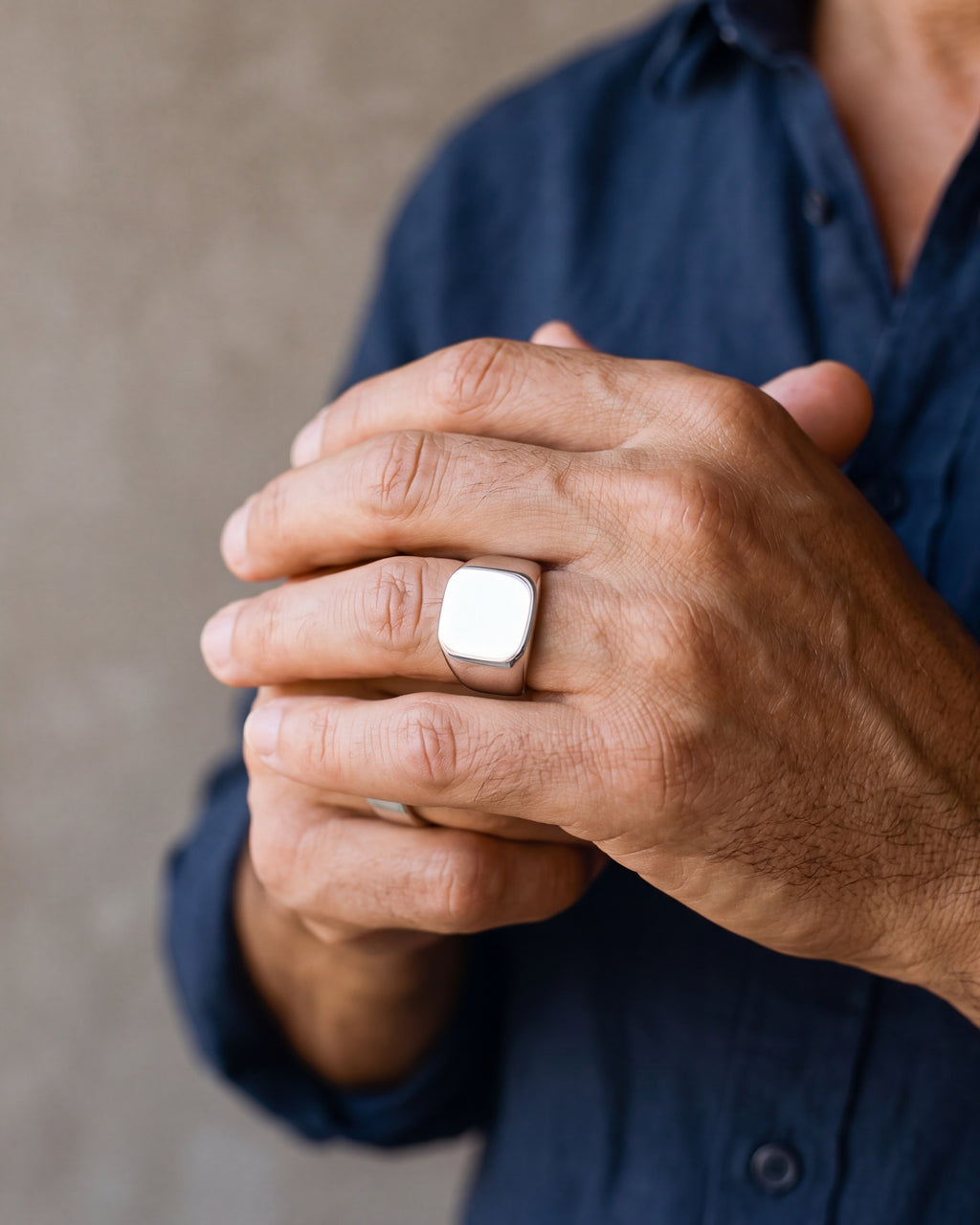 Close-up of a man's hands wearing the polished silver Atlas square signet ring at true size