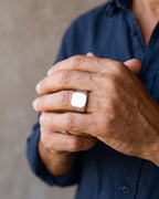 Close-up of a man's hands wearing the polished silver Atlas square signet ring at true size