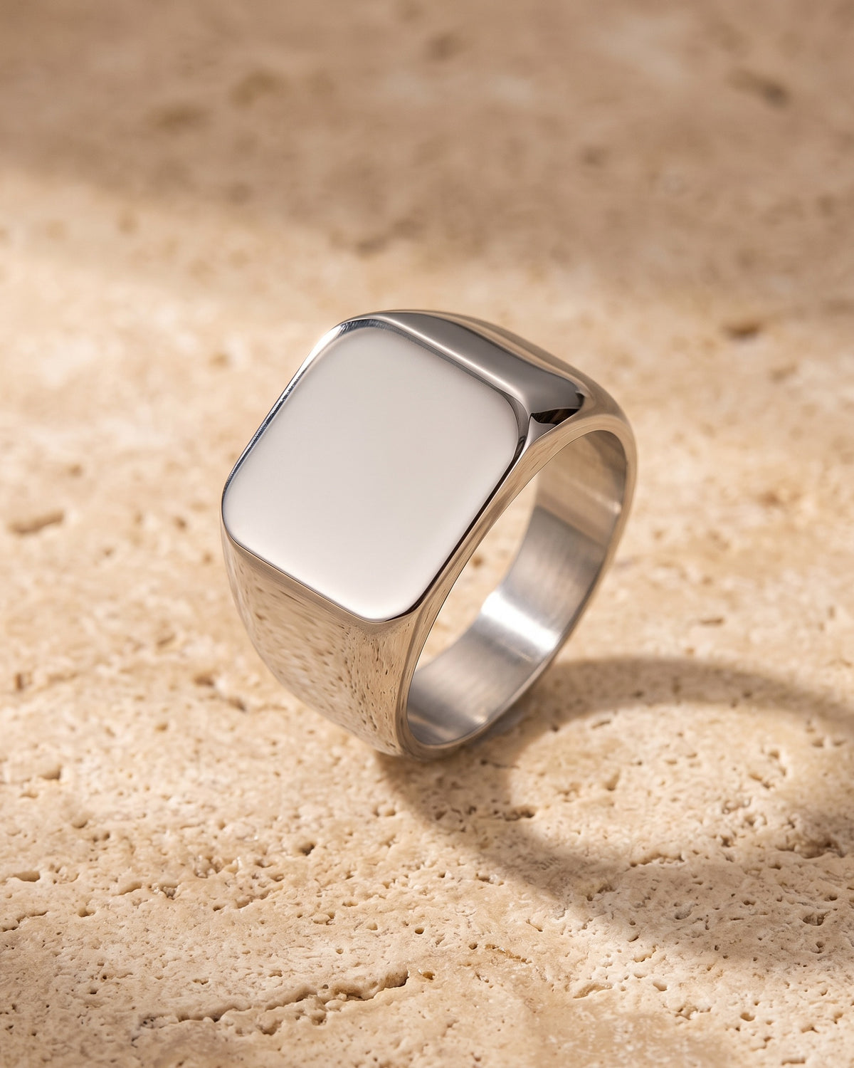 The polished silver Atlas square signet ring standing on warm stone