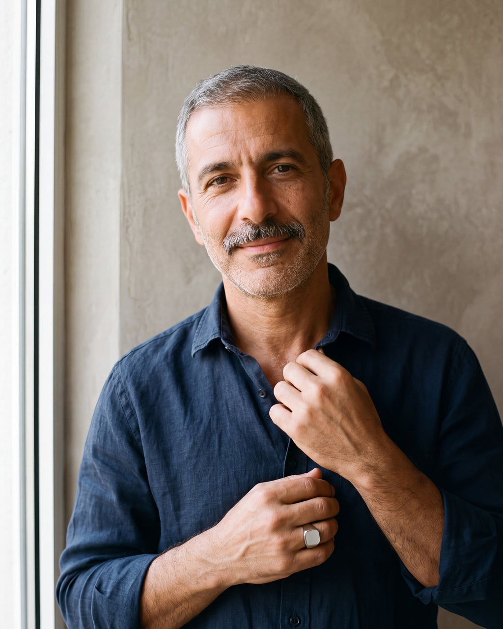 Man in a navy shirt by a window wearing the polished silver Atlas square signet ring