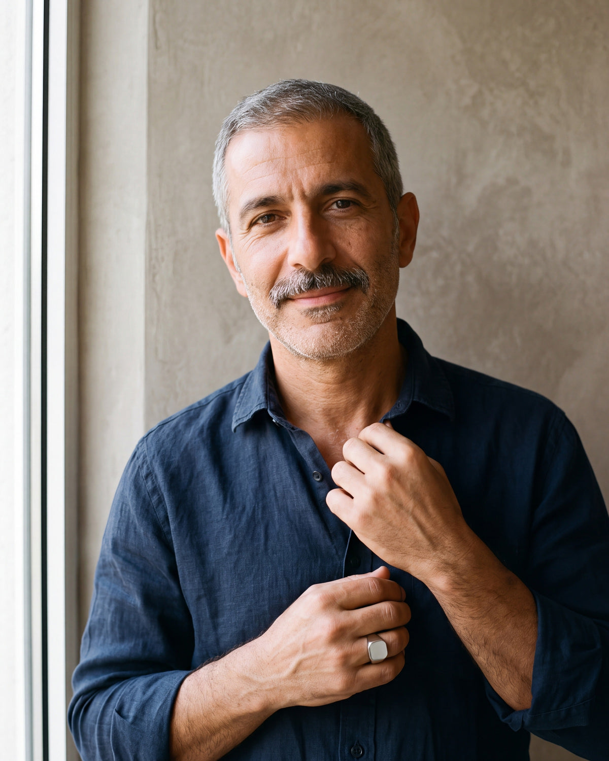 Man in a navy shirt by a window wearing the polished silver Atlas square signet ring