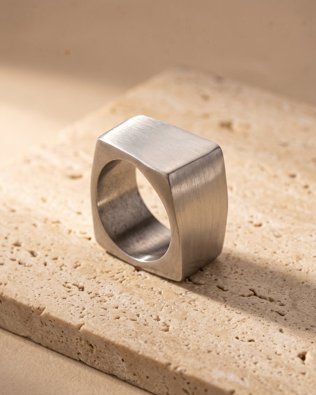 Entire Atlas square top ring in silver-tone steel, lying flat on warm stone