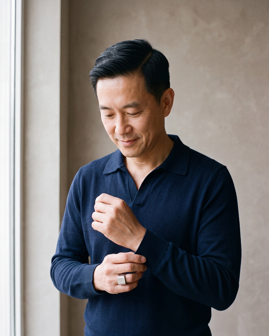 Man in a navy knit polo by a window wearing the Atlas square top ring in silver-tone steel