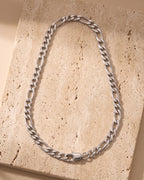 The whole silver-tone Atlas Figaro chain laid on warm stone, lobster clasp closed