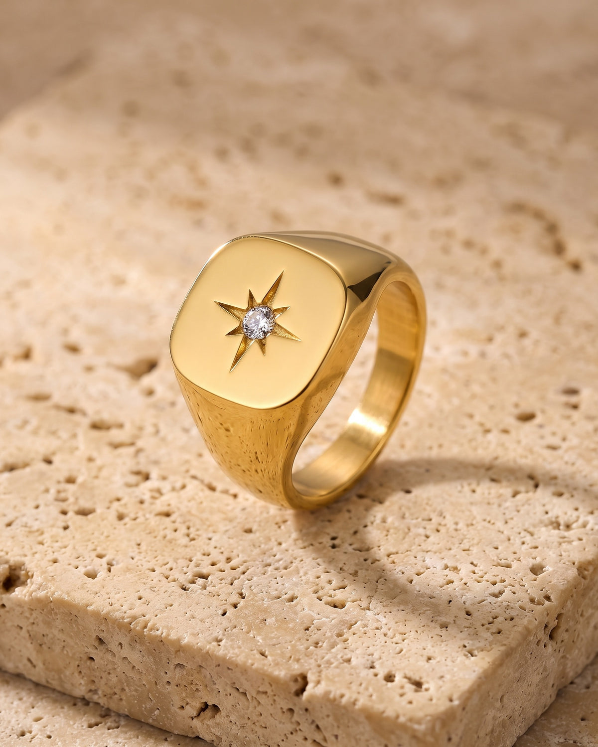 Atlas gold-tone star signet ring standing on warm stone