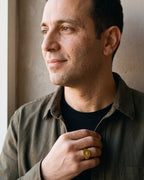 Man in an olive overshirt with his hand on his chest, wearing the Atlas gold-tone star signet ring