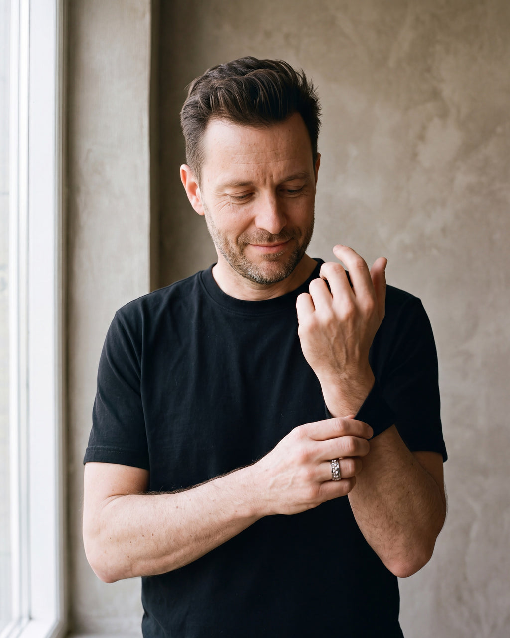 Man in a black T-shirt adjusting his sleeve wearing the silver-tone Atlas textured spinner ring