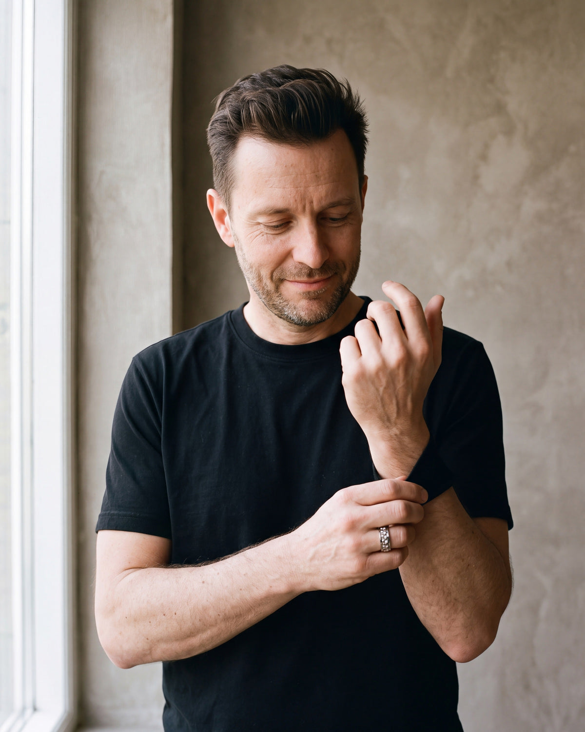 Man in a black T-shirt adjusting his sleeve wearing the silver-tone Atlas textured spinner ring