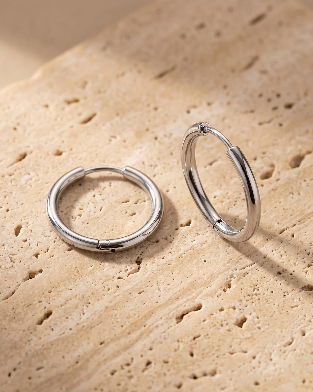 The whole silver-tone Atlas thin seamless hoop earrings laid on warm stone