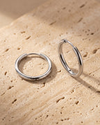 The whole silver-tone Atlas thin seamless hoop earrings laid on warm stone