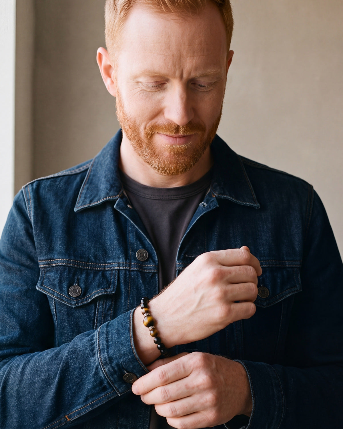 Man in a denim jacket adjusting his cuff, wearing the Atlas tiger eye bead bracelet