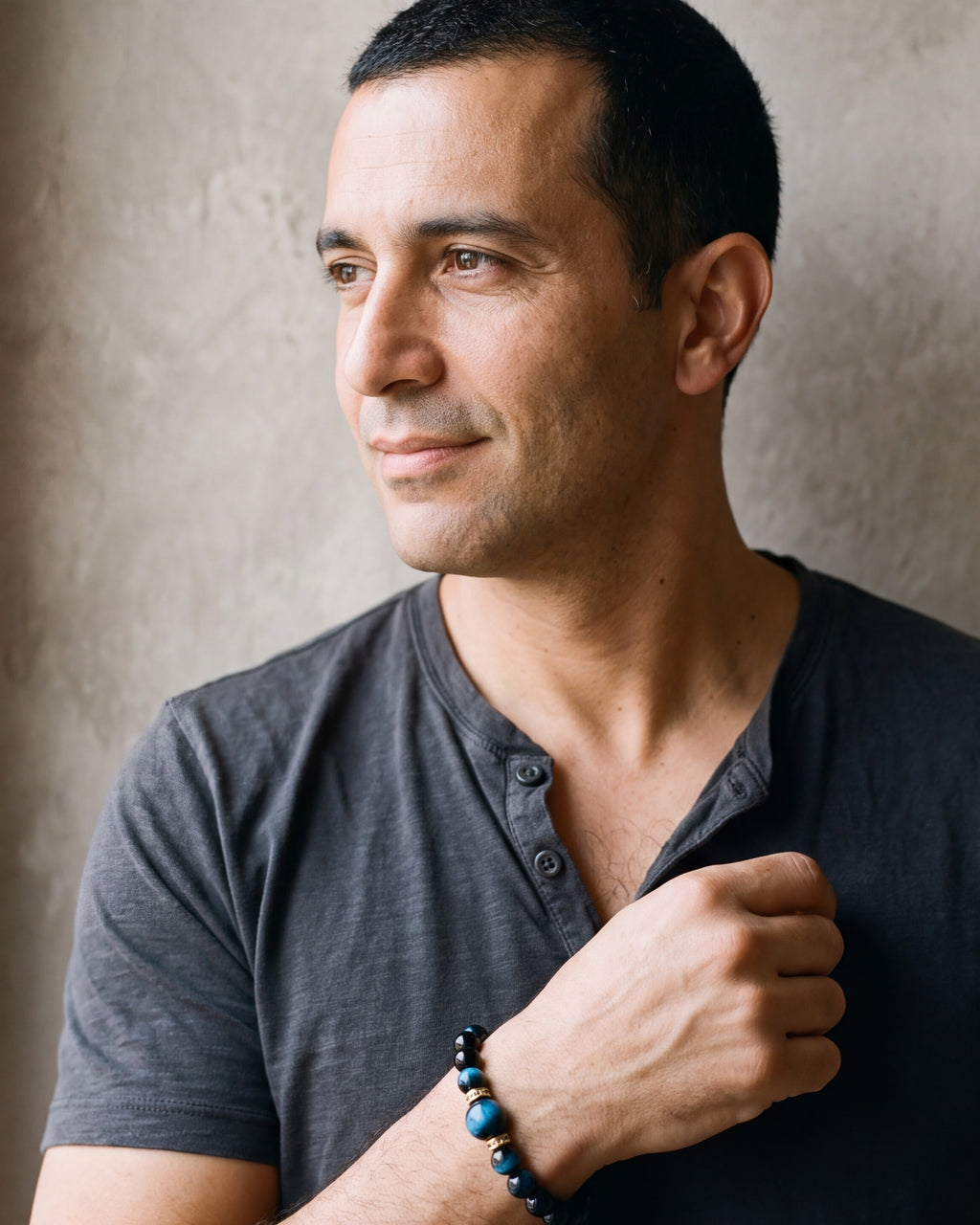 Man in a charcoal henley looking toward the window, wearing the Atlas blue tiger eye bead bracelet