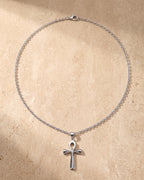 Entire Atlas ankh cross pendant necklace in silver-tone steel, lying flat on warm stone