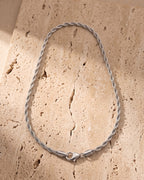 The silver Atlas Titanium Steel Rope Chain laid on warm travertine stone