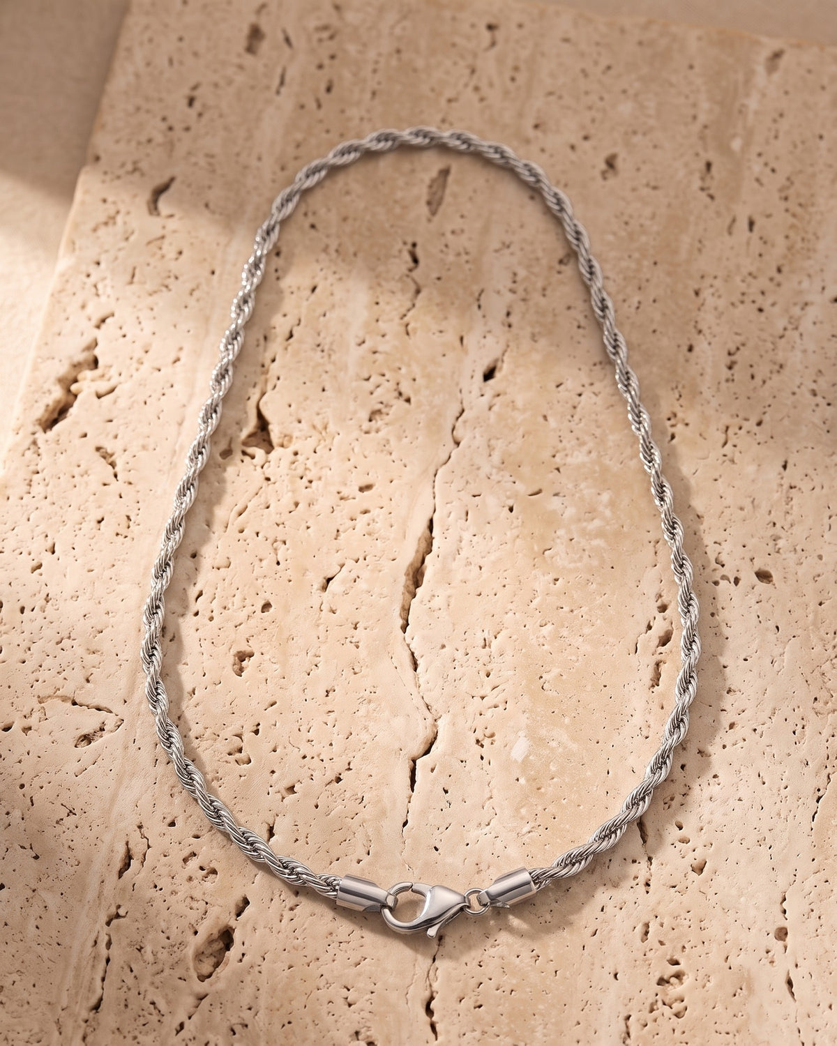 The silver Atlas Titanium Steel Rope Chain laid on warm travertine stone