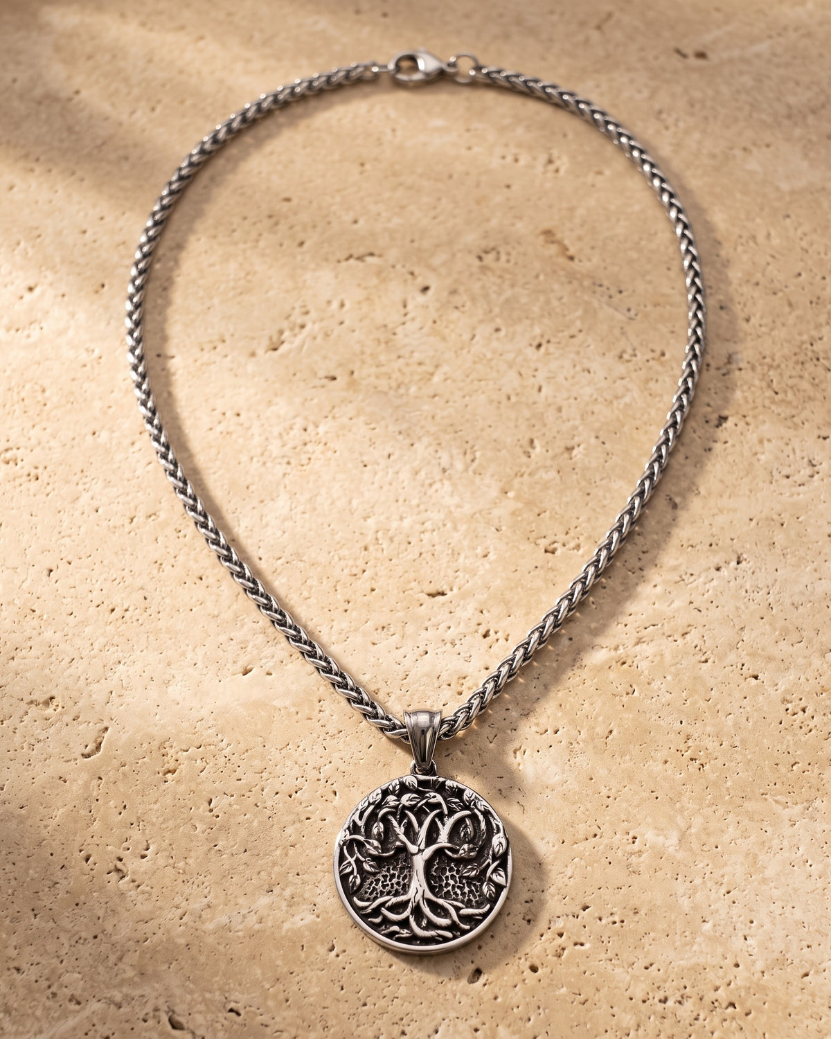Atlas Tree of Life pendant and wheat chain laid whole on warm stone