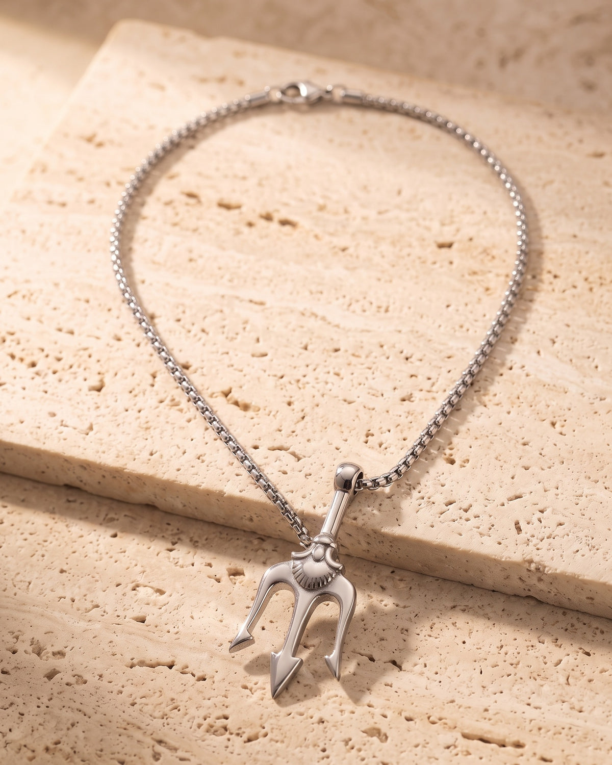 The whole silver-tone Atlas trident pendant necklace on warm stone