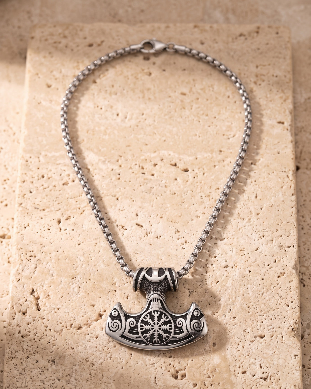 The whole silver-tone Atlas viking hammer pendant necklace lying on warm travertine stone