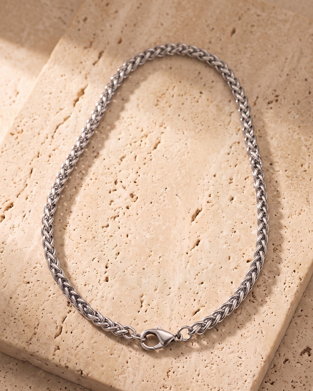 The whole silver-tone Atlas wheat chain laid on warm stone, lobster clasp closed