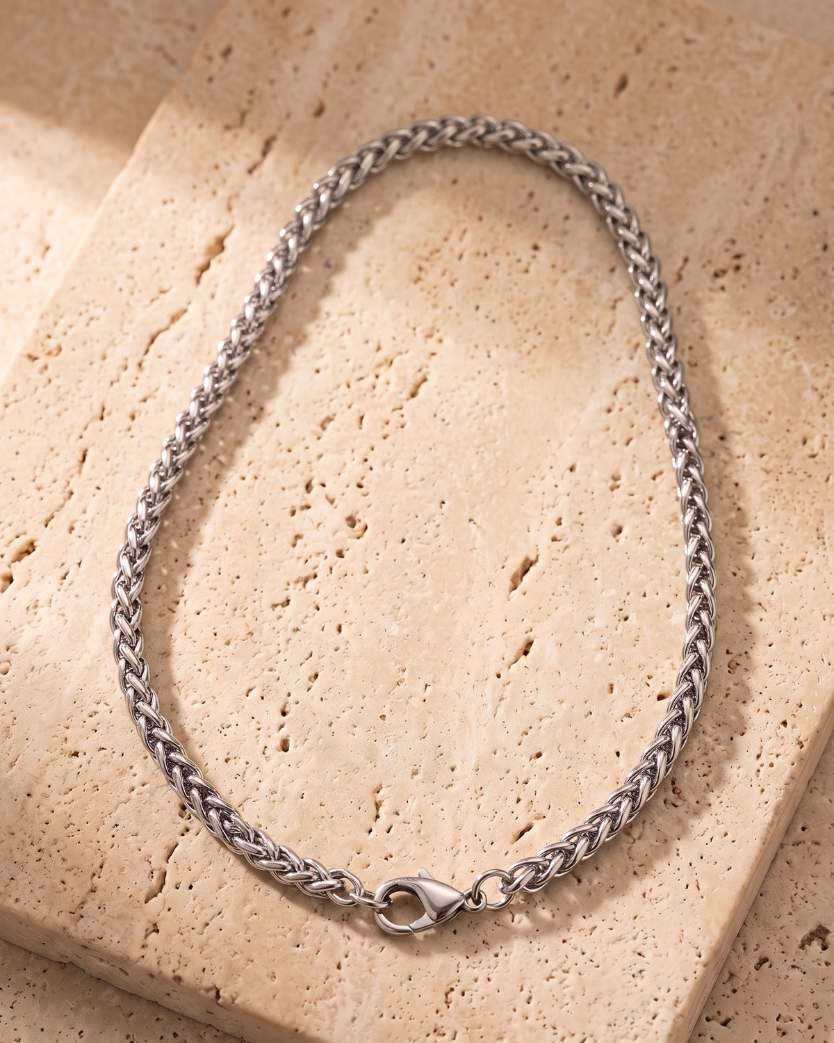 The whole silver-tone Atlas wheat chain laid on warm stone, lobster clasp closed