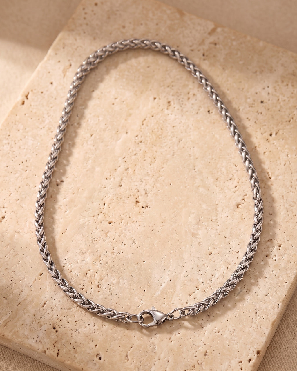 Entire Atlas wheat chain in silver-tone steel, lying flat on warm stone