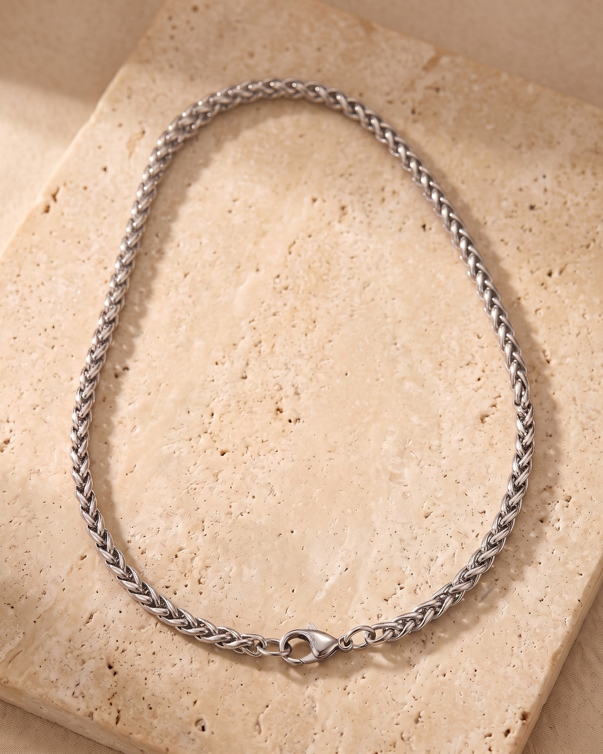Entire Atlas wheat chain in silver-tone steel, lying flat on warm stone