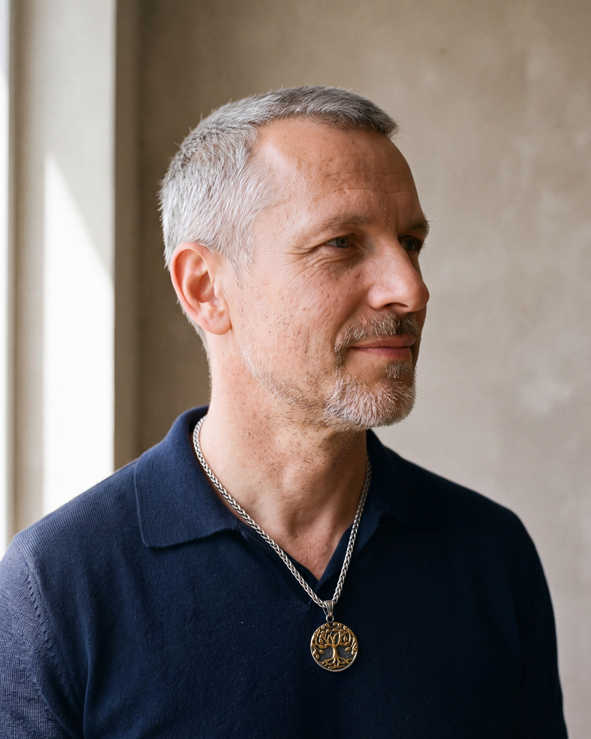 Man in a navy knit polo by a window wearing the Atlas two-tone tree of life pendant necklace