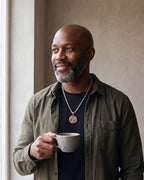 Man in an olive overshirt holding a coffee cup, wearing the Atlas tree of life pendant necklace