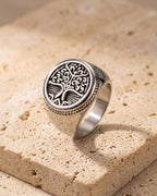 The whole silver-tone Atlas tree of life signet ring lying on warm travertine stone