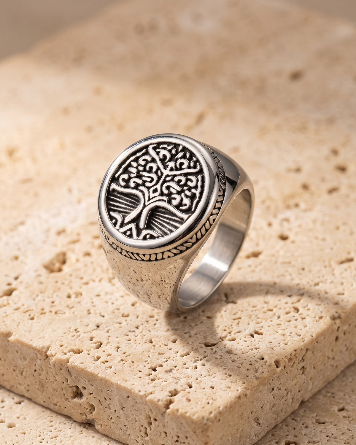 The whole silver-tone Atlas tree of life signet ring lying on warm travertine stone