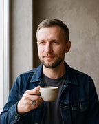 Man in a dark indigo denim jacket open over a charcoal crew-neck t-shirt by a window wearing the silver-tone Atlas tree of life signet ring