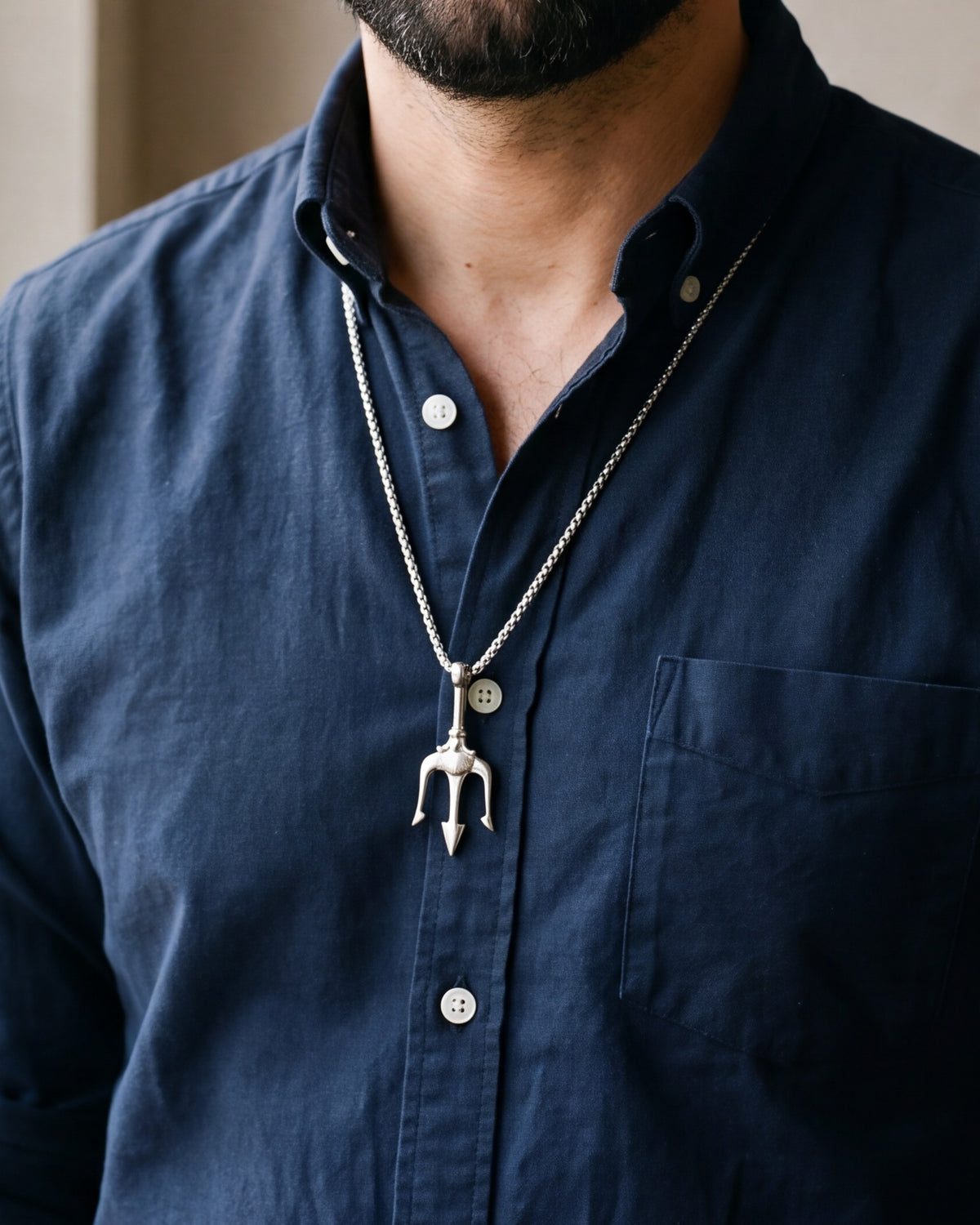 Close-up of the silver Atlas trident pendant worn on a navy shirt