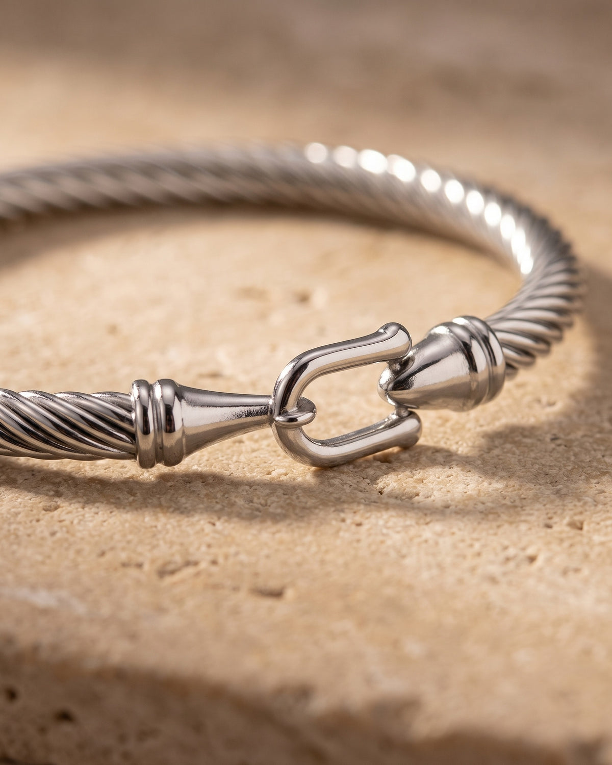 Close-up of the silver Atlas twisted cable bangle horseshoe clasp on warm stone